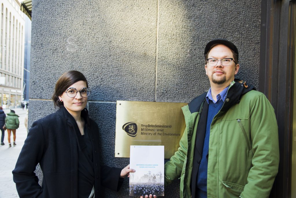 Kuvassa on Paloma Hannonen ja Harri Hölttä, jotka seisovat ympäristöministeriön kyltin edessä pitäen suovetoomusta. Kuva: Oona Lohilahti