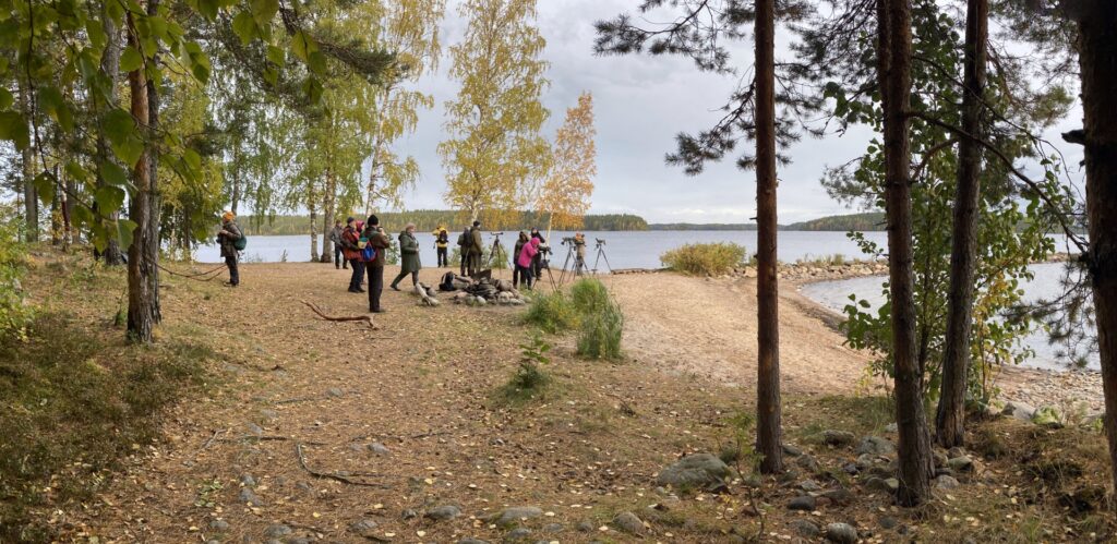 Syksyinen hiekkaranta, jossa ihmisiä katsomassa järvelle. 