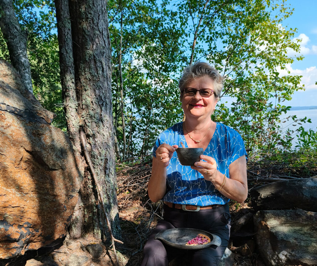 Retkeilyastioihin erikoistuneen Kupilka-yrityksen toimitusjohtaja Arja Kaasinen istuu metsässä. Kädessään hänellä on kuppi.