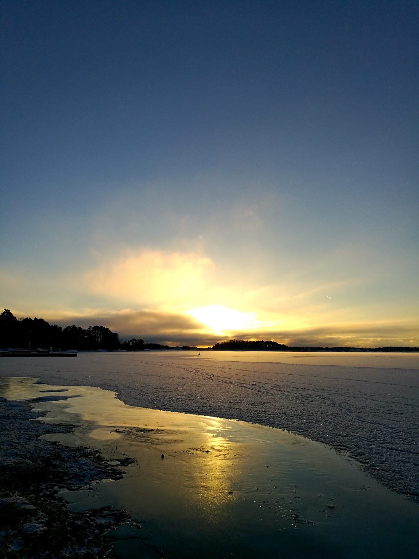 Aurinko laskee meren rannalla talvisena päivänä.