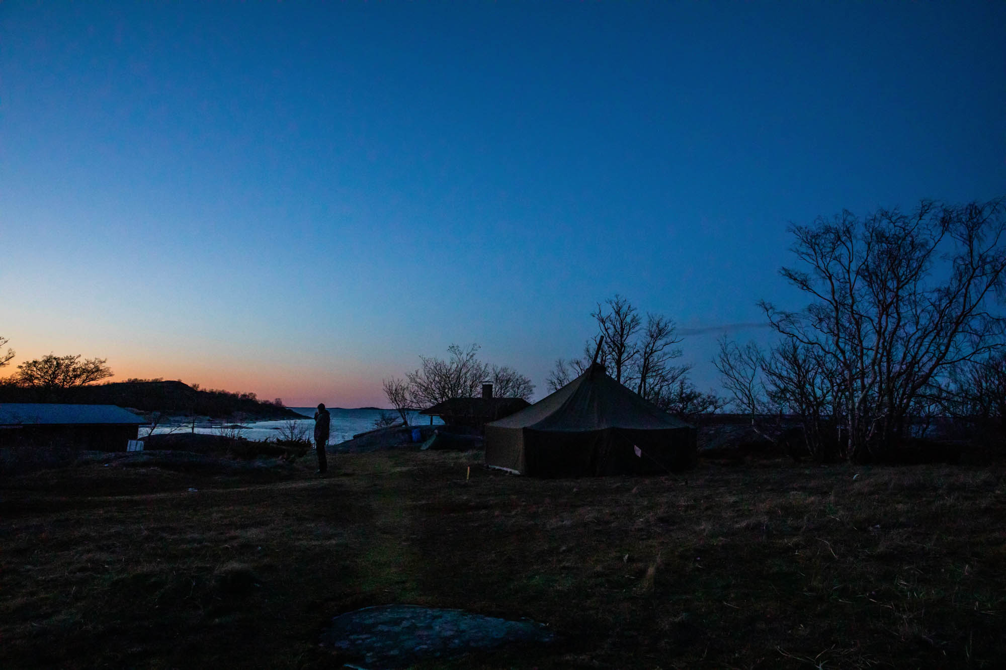 Kuvassa näkyy puolijoukkuteltta ja taivaanrannassa auringonlaskun värjäämää taivasta.