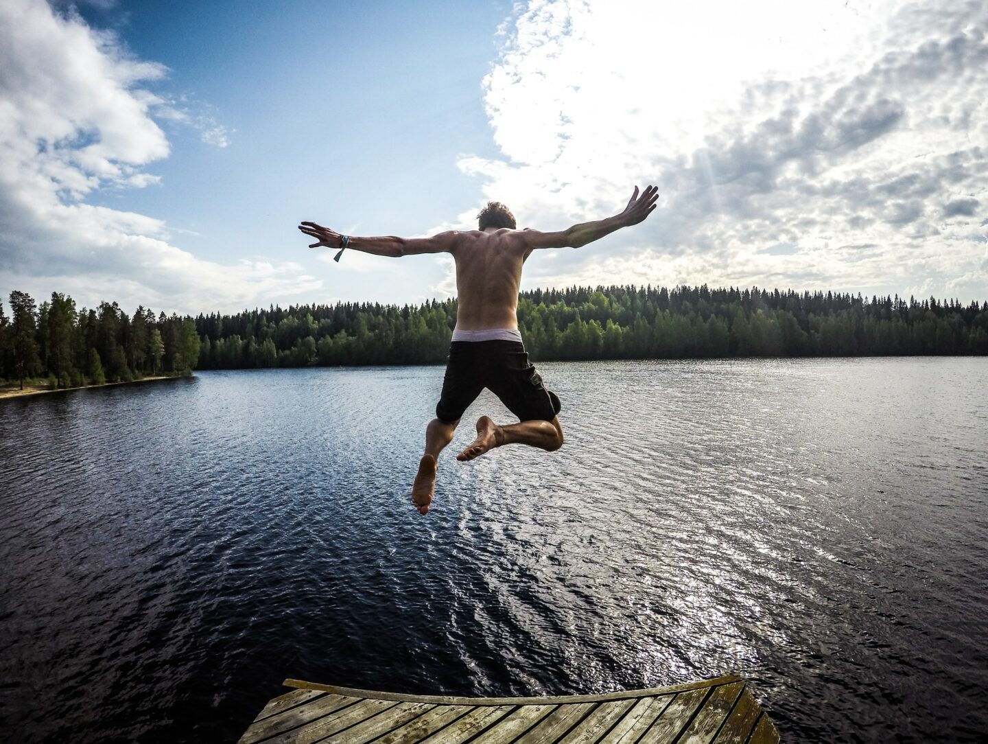 A man jumping into a Finnish lake during summer time, sun is shining in the background.